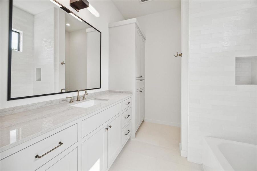 This bathroom showcases a crisp, white design with a long vanity topped with a polished stone surface. A large mirror framed in black adds contrast, while brass fixtures provide a touch of elegance. The shower/tub combo, clad in white subway tiles, features a convenient built-in niche, emphasizing the clean and functional aesthetic.