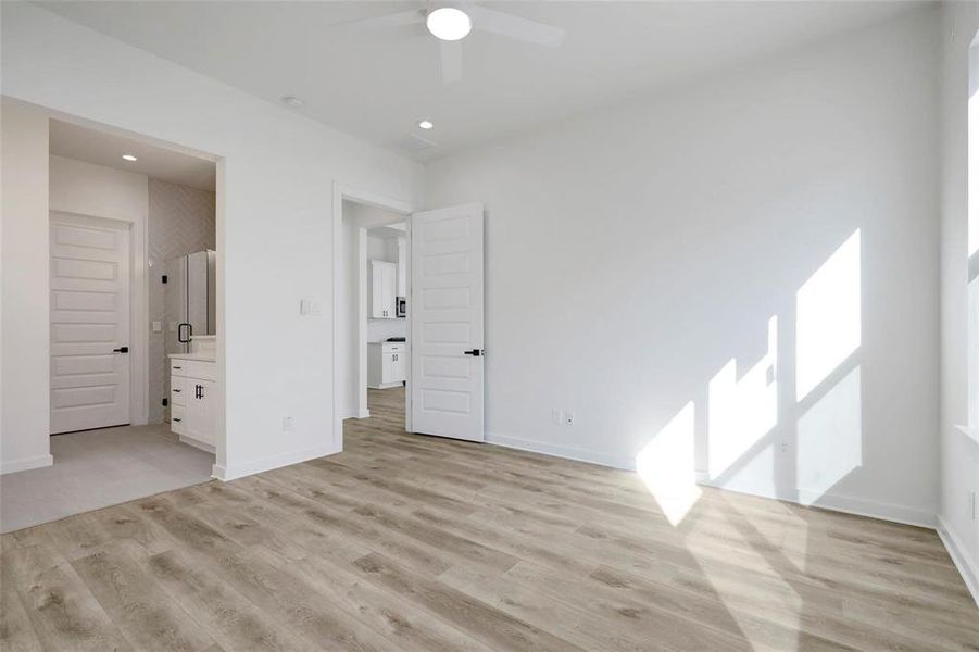 A minimalist white room with elegant hardwood flooring and a ceiling fan, enhancing the room's openness and comfort.