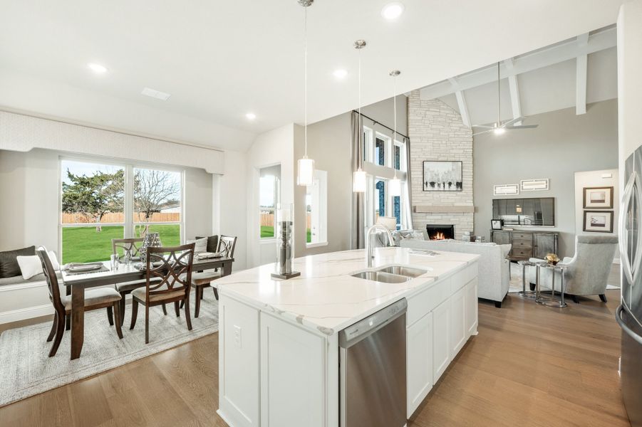 Open-concept kitchen with white island, quartz countertops, and views into dining and living areas with stone fireplace. Open-concept kitchen with white island, quartz countertops, and views into dining and living areas with stone fireplace.
