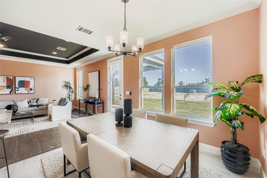Dining space featuring crown molding, light wood finished floors, a chandelier, and a raised ceiling