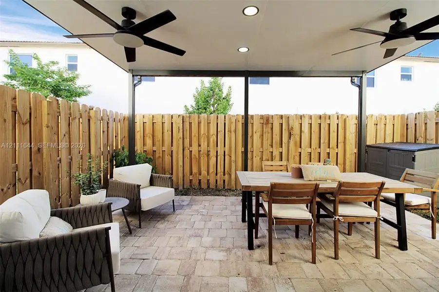 Covered patio featuring a paver surface, recessed lighting, two ceiling fans, and a wood privacy fence Covered patio featuring a paver surface, recessed lighting, two ceiling fans, and a wood privacy fence