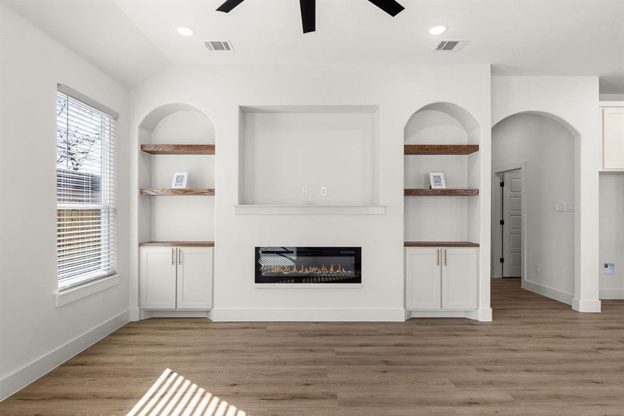 Unfurnished living room featuring ceiling fan, lofted ceiling, light hardwood / wood-style floors, and built in shelves