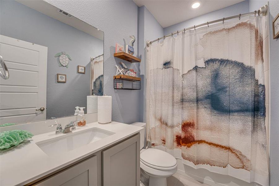 Bathroom with a textured wall, vanity, and shower / bath combo with shower curtain