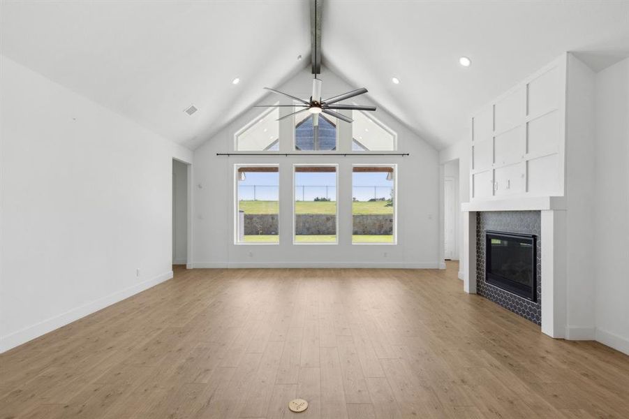 Unfurnished living room featuring light wood-type flooring, beamed ceiling, ceiling fan, and high vaulted ceiling