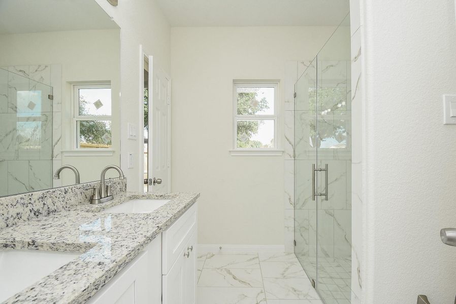 A modern bathroom with marble walls, glass shower enclosure, granite countertop, and two windows letting in natural light. A modern bathroom with marble walls, glass shower enclosure, granite countertop, and two windows letting in natural light.