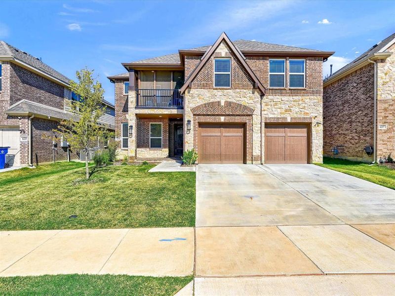 View of front facade featuring a front yard, a balcony, and a garage View of front facade featuring a front yard, a balcony, and a garage