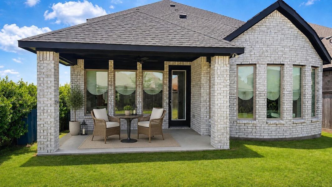 A covered back patio includes a concrete floor, brick pillars, a ceiling fan, and a glass door. Multiple windows look out onto the backyard lawn.**This room has been virtually staged.