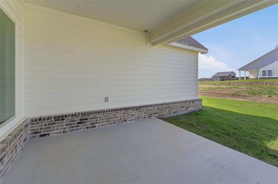 Covered concrete patio with white horizontal siding and a brick skirting