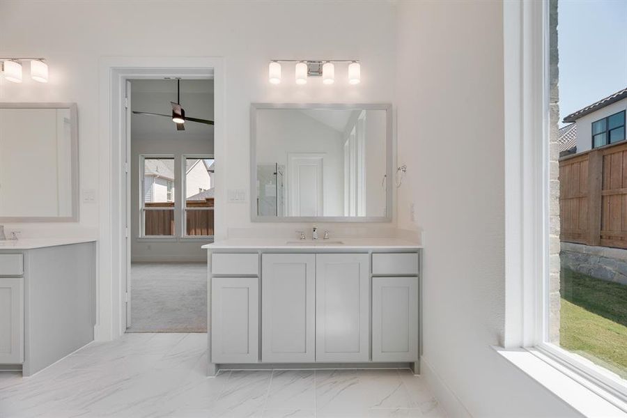 Bathroom with light marble finish floors, two vanities, ceiling fan, and a shower