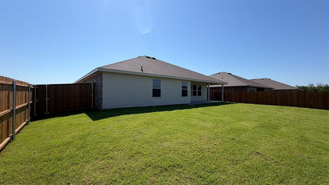Spacious backyard featuring a manicured lawn, full perimeter wood fencing, and a covered patio area Spacious backyard featuring a manicured lawn, full perimeter wood fencing, and a covered patio area