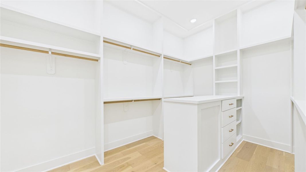 Very spacious, well-lit walk-in primary closet filled with shelving and hanging space, featuring a central island with drawers.