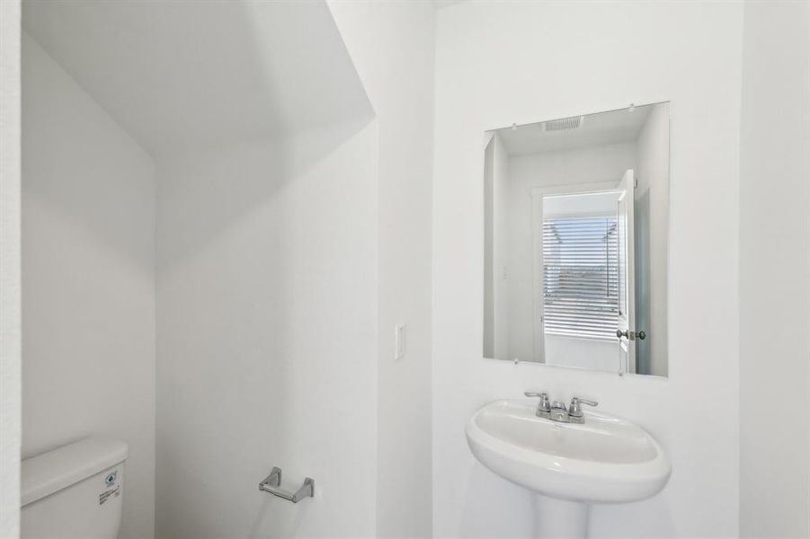 Bathroom featuring a pedestal sink with chrome fixtures, a wall-mounted mirror, and a white toilet
