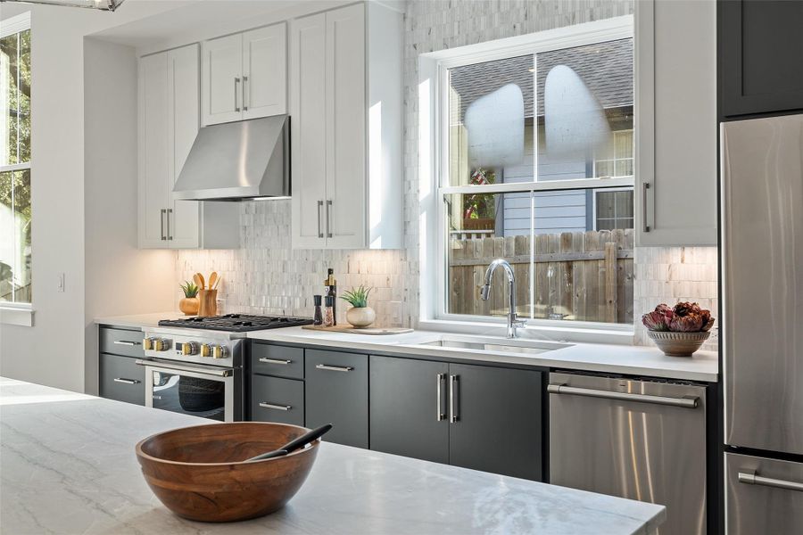 Kitchen with appliances with stainless steel finishes, extractor fan, sink, backsplash, and gray cabinets