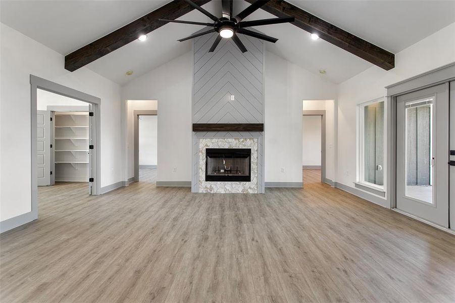 Unfurnished living room featuring beamed ceiling, light hardwood / wood-style flooring, a fireplace, and ceiling fan