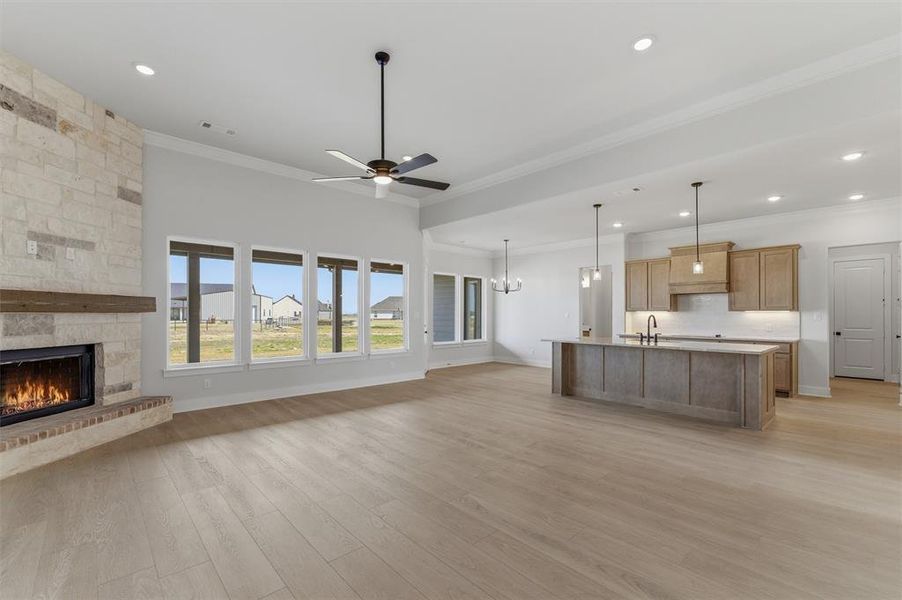Unfurnished living room with ceiling fan, a stone fireplace, light wood-style floors, ornamental molding, and hanging lights Unfurnished living room with ceiling fan, a stone fireplace, light wood-style floors, ornamental molding, and hanging lights