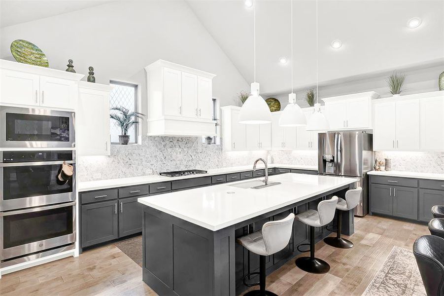 Kitchen featuring white cabinets, a kitchen breakfast bar, gray cabinetry, pendant lighting, and stainless steel appliances Kitchen featuring white cabinets, a kitchen breakfast bar, gray cabinetry, pendant lighting, and stainless steel appliances