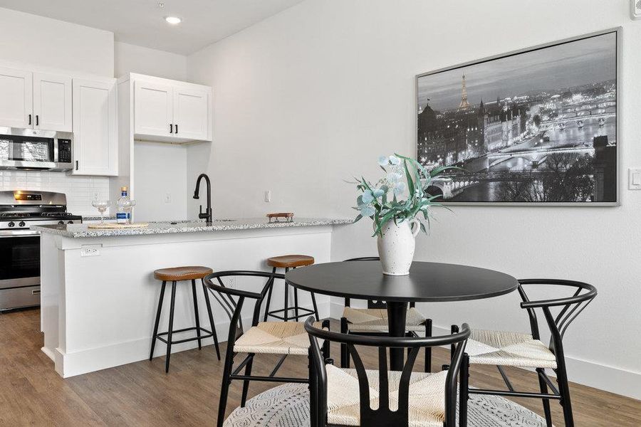 Kitchen featuring appliances with stainless steel finishes, white cabinetry, tasteful backsplash, light wood finished floors, and light stone counters
