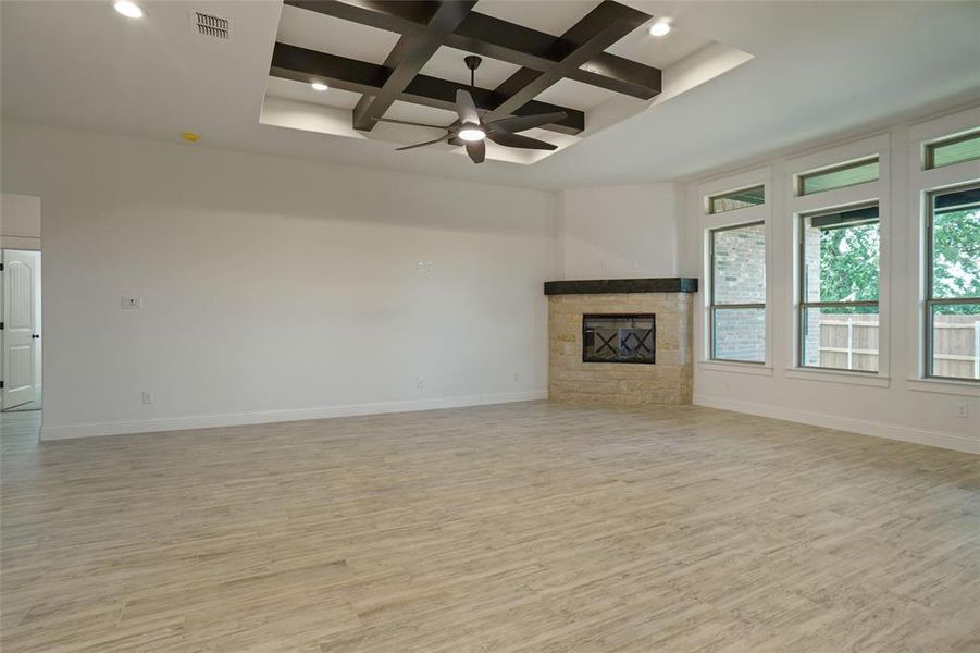 Unfurnished living room featuring coffered ceiling, light hardwood / wood-style flooring, ceiling fan, a stone fireplace, and beam ceiling