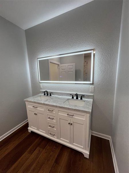 Bathroom with a textured wall, double vanity, and dark wood-type flooring Bathroom with a textured wall, double vanity, and dark wood-type flooring
