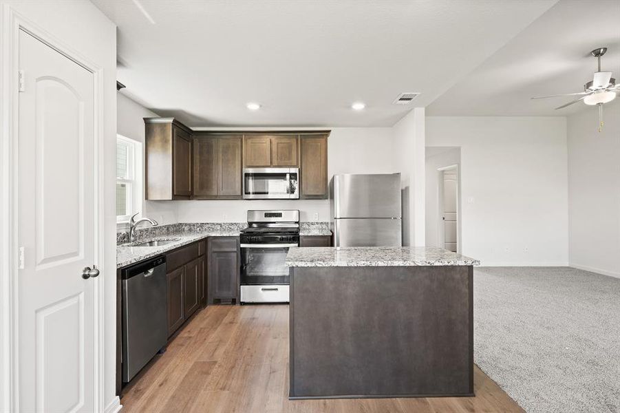 Kitchen featuring light colored carpet, a center island, sink, light stone countertops, and stainless steel appliances