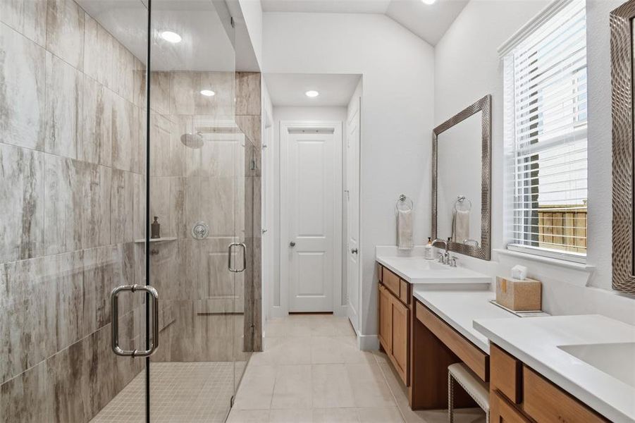 Spacious bathroom featuring a glass-enclosed shower with ceramic tile surround, dual vanity with undermount sinks, light wood-finish cabinetry, and white countertops Spacious bathroom featuring a glass-enclosed shower with ceramic tile surround, dual vanity with undermount sinks, light wood-finish cabinetry, and white countertops