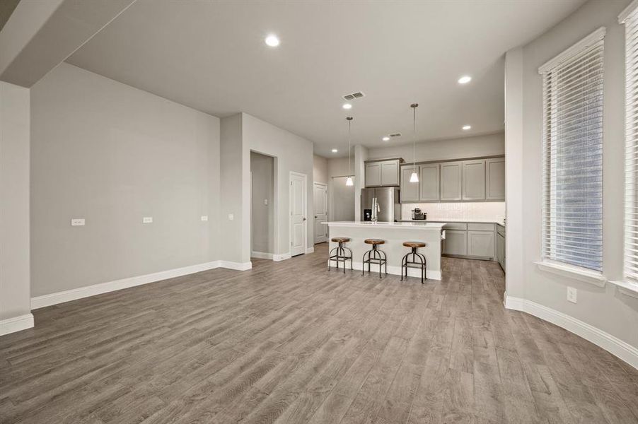 Another angle of the open dining and kitchen space, highlighting pendant lighting, breakfast bar seating, and wood-look tile flooring.