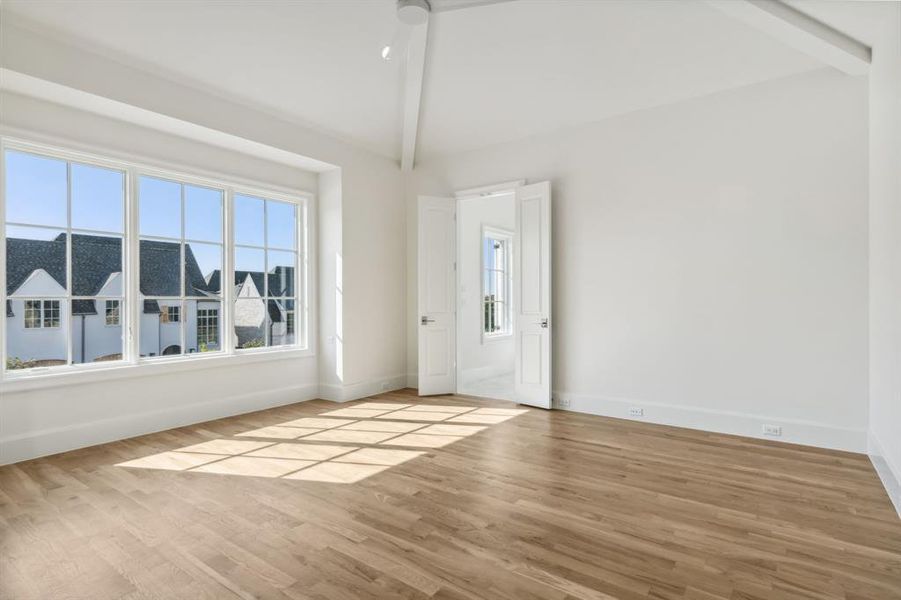 Primary bedroom with lofted ceiling with beams and light hardwood floors