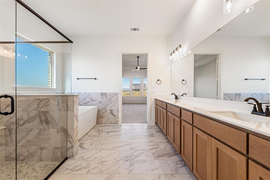 Bathroom with a freestanding tub, light marble finish floors, double vanity, a stall shower, and ceiling fan
