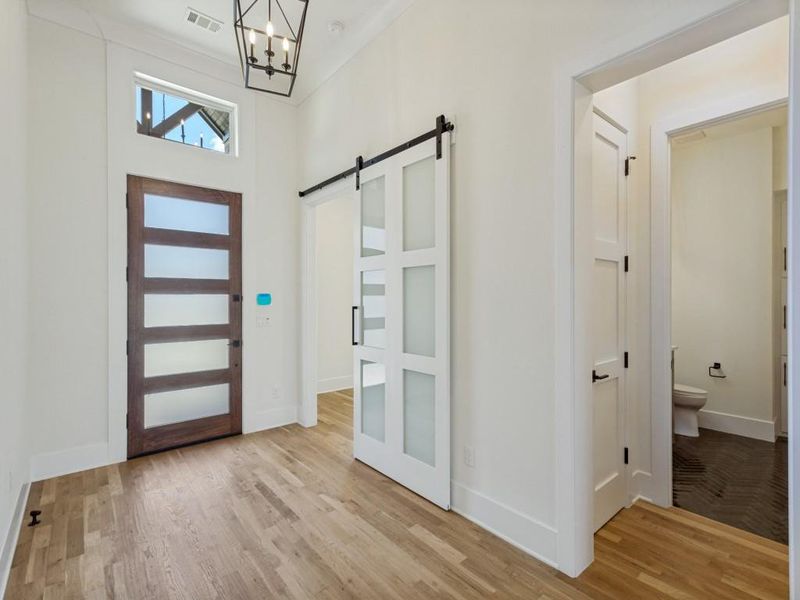 Entryway featuring wood-finish flooring, a contemporary dark wood entry door with frosted panels, and an overhead transom window Entryway featuring wood-finish flooring, a contemporary dark wood entry door with frosted panels, and an overhead transom window