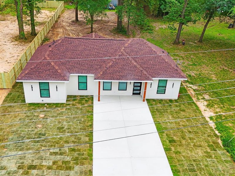 Modern single-story residence featuring a white exterior with black-framed windows, a red shingle roof, and a prominent concrete driveway Modern single-story residence featuring a white exterior with black-framed windows, a red shingle roof, and a prominent concrete driveway