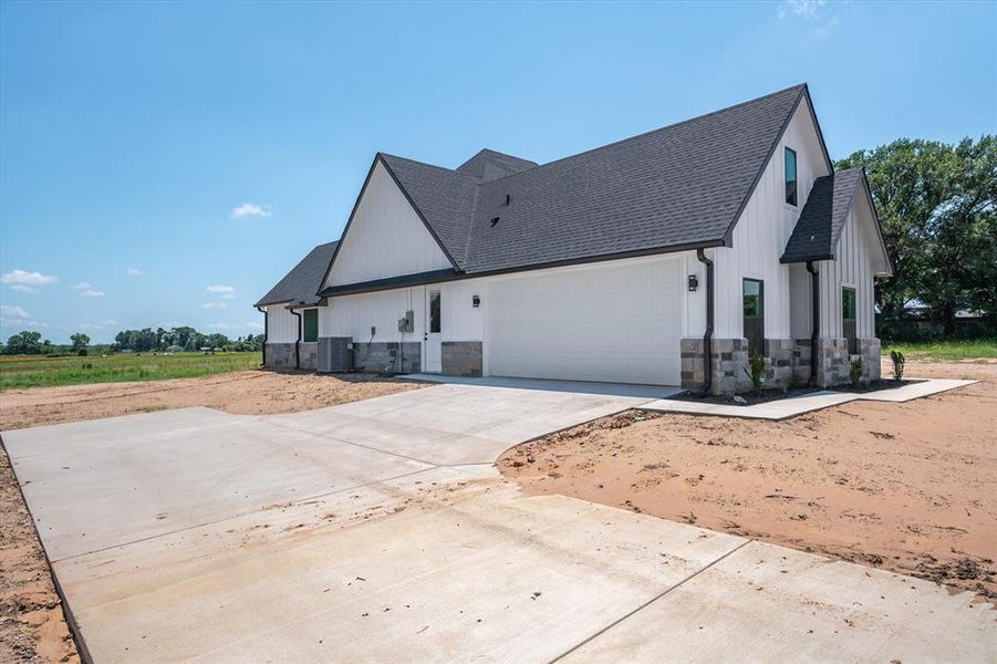 View of home's exterior featuring stone siding, concrete driveway, a shingled roof, and a garage