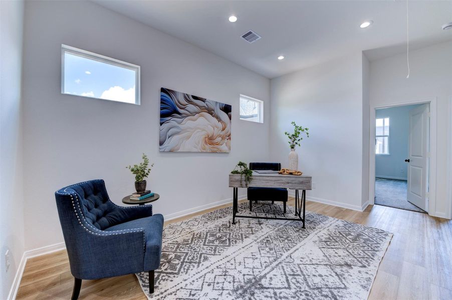 Flex room set up as home office with hardwood floors, high ceilings, clerestory windows for natural light, and open sightlines to hallway.