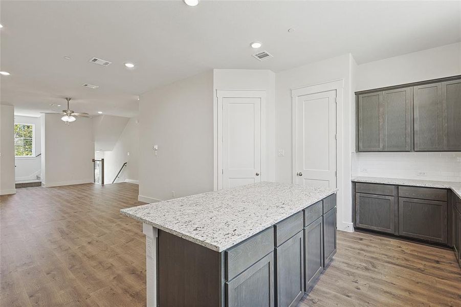 Kitchen featuring ceiling fan, a center island, tasteful backsplash, light stone counters, and wood-type flooring