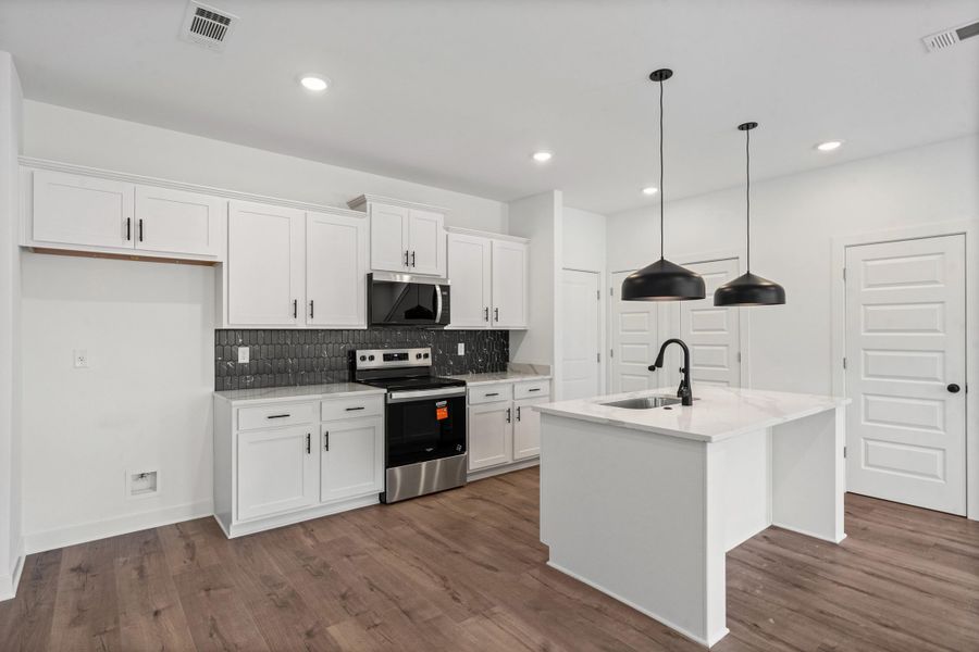 Modern kitchen featuring white cabinetry, a dark tiled backsplash, stainless steel appliances, a center island with a sink, and wood-finish flooring Modern kitchen featuring white cabinetry, a dark tiled backsplash, stainless steel appliances, a center island with a sink, and wood-finish flooring