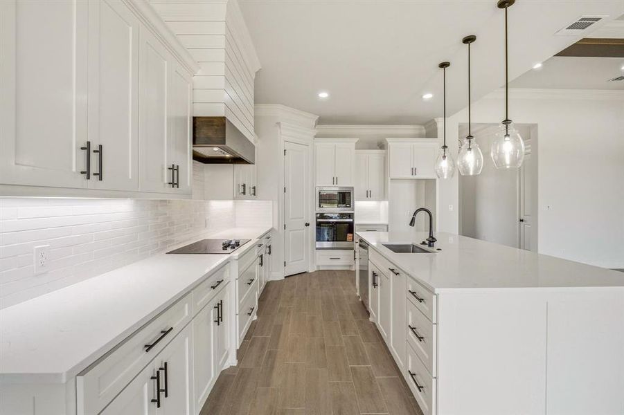 Kitchen with an island with sink, white cabinets, stainless steel appliances, wood finish floors, and decorative backsplash