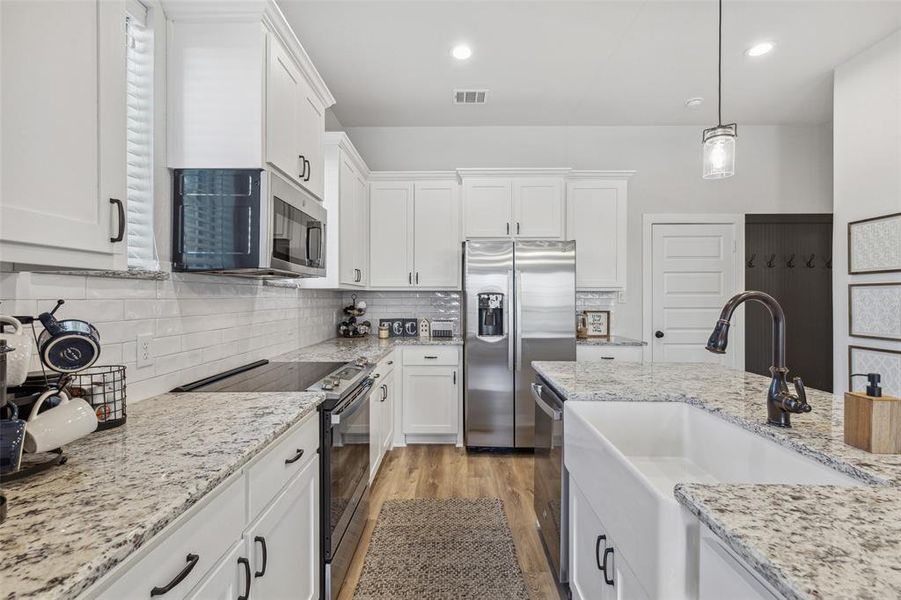 Kitchen featuring backsplash, white cabinetry, light wood-type flooring, and stainless steel appliances