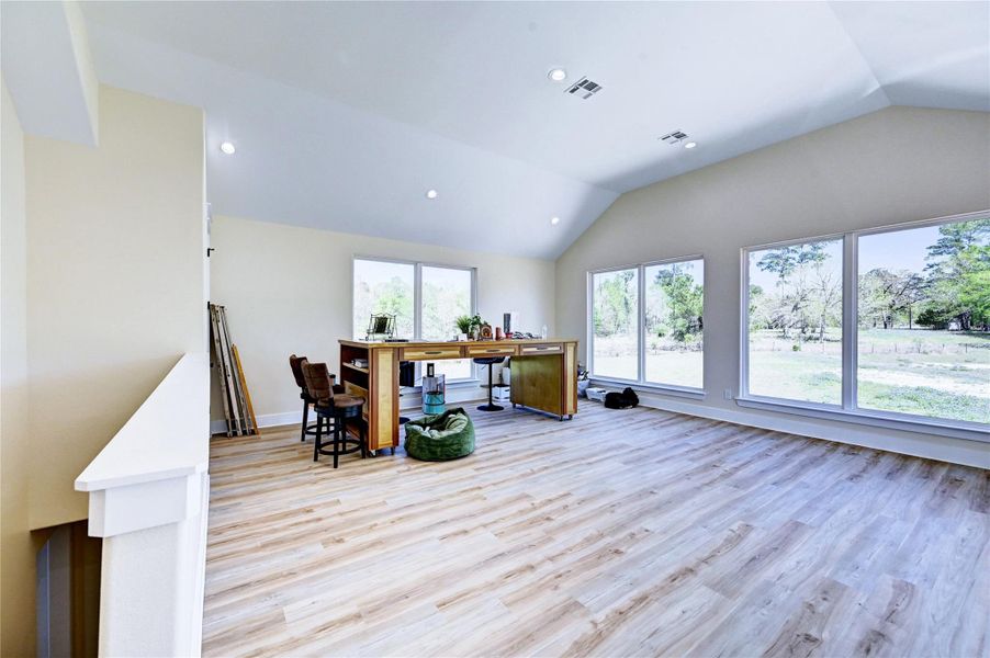 Bright and spacious room with large windows offering scenic outdoor views, wood flooring, and high ceilings. Ideal for a home office or creative space.