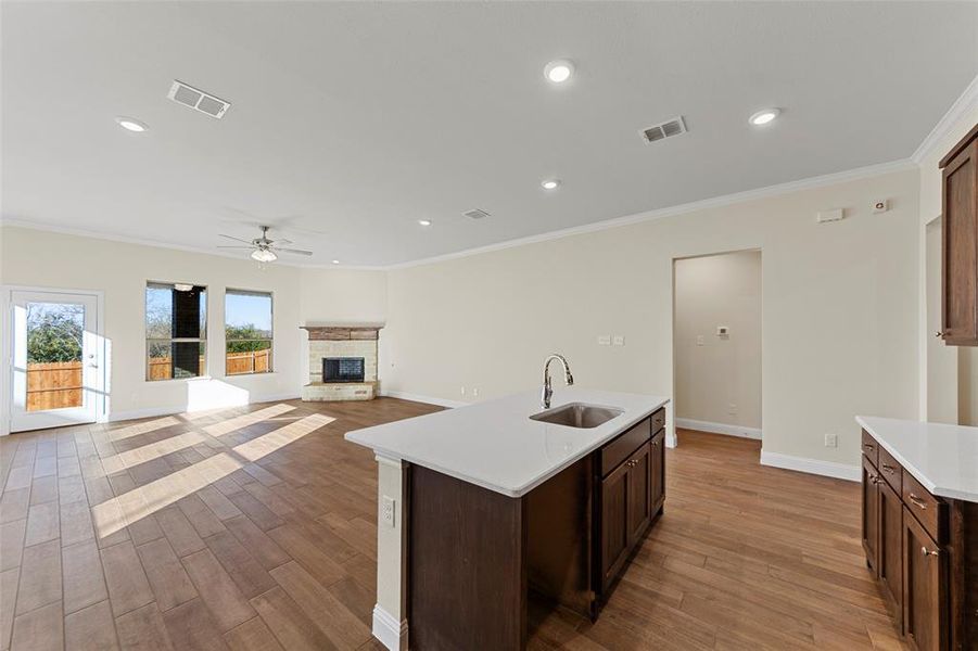 Kitchen with ceiling fan, sink, a center island with sink, light hardwood / wood-style floors, and a stone fireplace