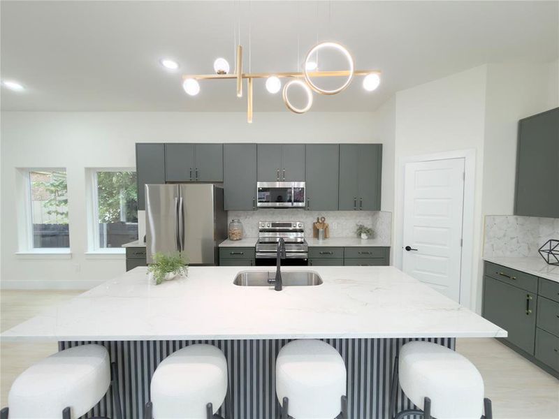 Kitchen featuring light stone countertops, a kitchen breakfast bar, appliances with stainless steel finishes, tasteful backsplash, and a kitchen island with sink