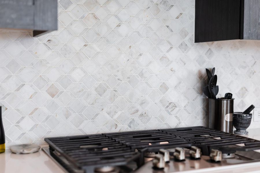 Kitchen view of stainless steel gas stovetop, decorative backsplash, and light stone counters