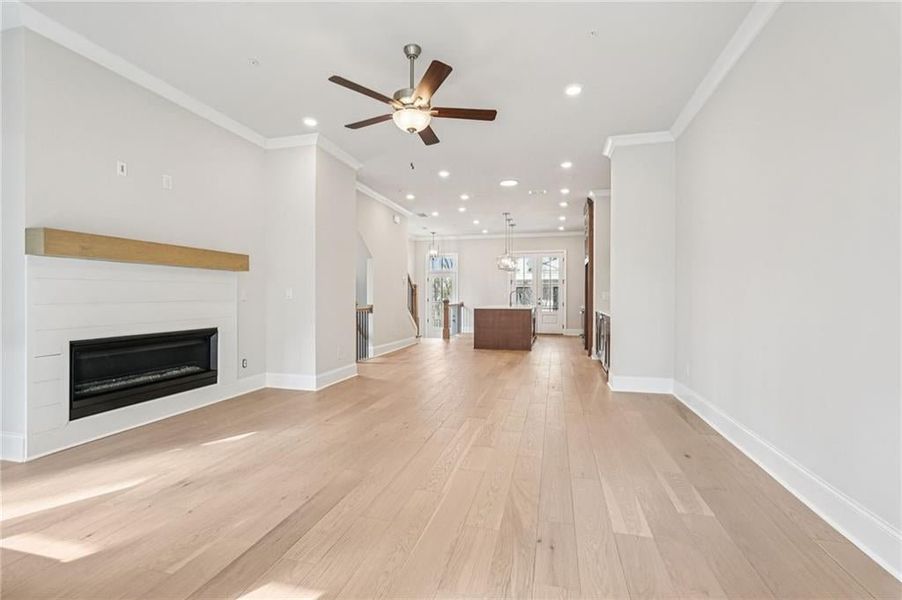 Unfurnished living room featuring a glass covered fireplace, light wood-type flooring, a ceiling fan, recessed lighting, and crown molding