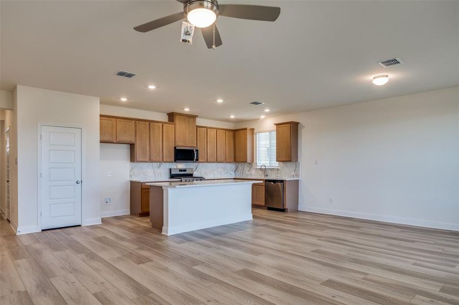 Kitchen with light countertops, light wood-style flooring, stainless steel appliances, ceiling fan, and brown cabinets