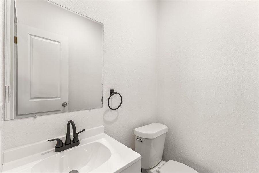 Bathroom featuring a white vanity with integrated sink, black faucet, wall-mounted mirror, and white commode