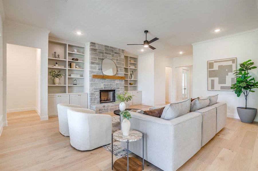 Living area with built in adjustable shelves, light engineered wood flooring, a stone fireplace with solid cedar mantle, ceiling fan, and french doors that open to a covered back patio. Living area with built in adjustable shelves, light engineered wood flooring, a stone fireplace with solid cedar mantle, ceiling fan, and french doors that open to a covered back patio.