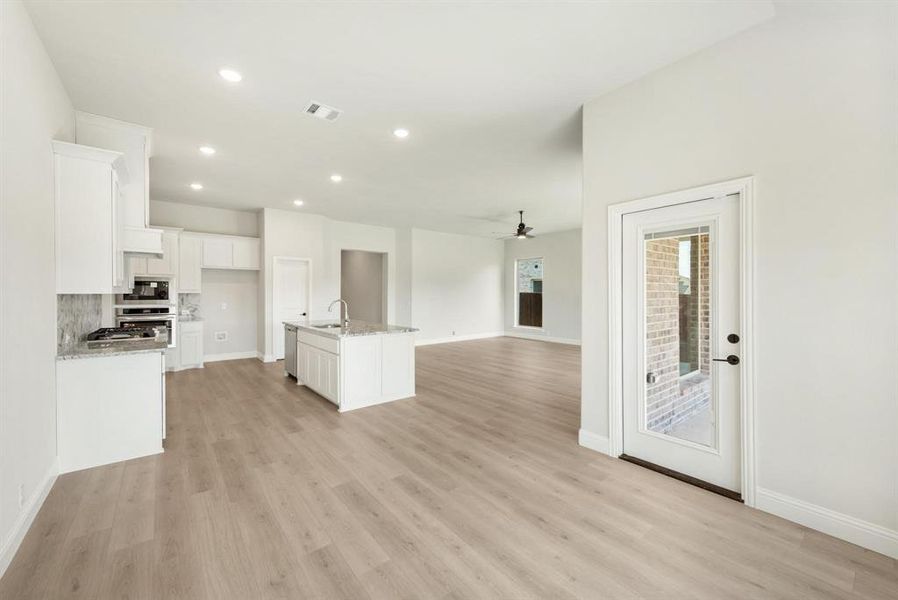 Open-concept kitchen and living area featuring wood-finish flooring, recessed lighting, and a white cabinetry kitchen with an island, granite countertops, and built-in appliances Open-concept kitchen and living area featuring wood-finish flooring, recessed lighting, and a white cabinetry kitchen with an island, granite countertops, and built-in appliances