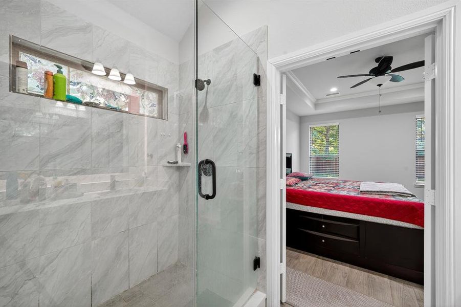 Full bath with ensuite bathroom, a shower stall, light wood-type flooring, ceiling fan, and crown molding