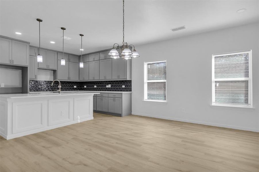 Kitchen with gray cabinetry, decorative backsplash, light wood-type flooring, recessed lighting, and decorative light fixtures