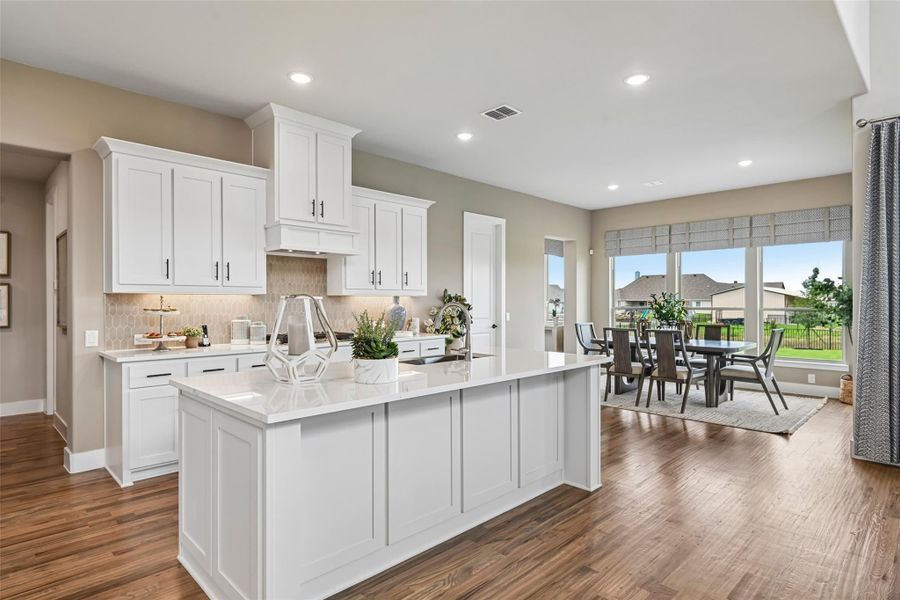 Open kitchen with white cabinets, large island, quartz countertops, and hardwood floors leading to dining area. Open kitchen with white cabinets, large island, quartz countertops, and hardwood floors leading to dining area.