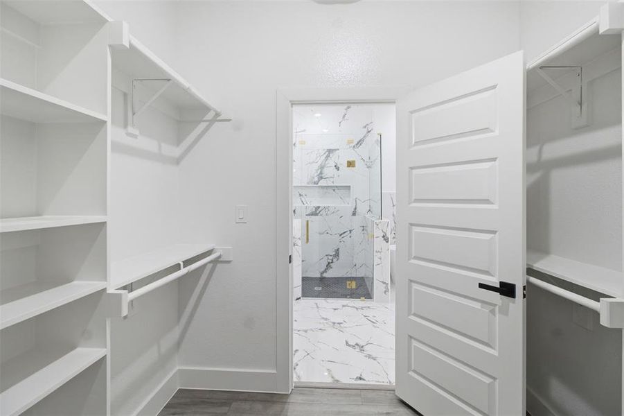 Walk-in closet featuring white built-in shelving, hanging rods, and wood-finish flooring