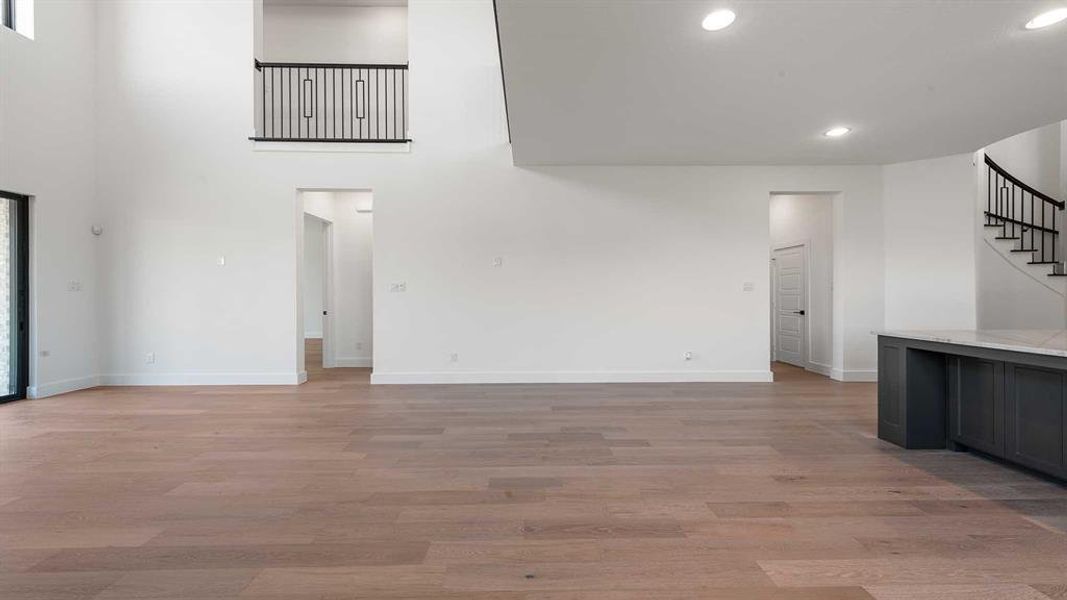 Unfurnished living room featuring stairs, recessed lighting, light wood finished floors, and a towering ceiling